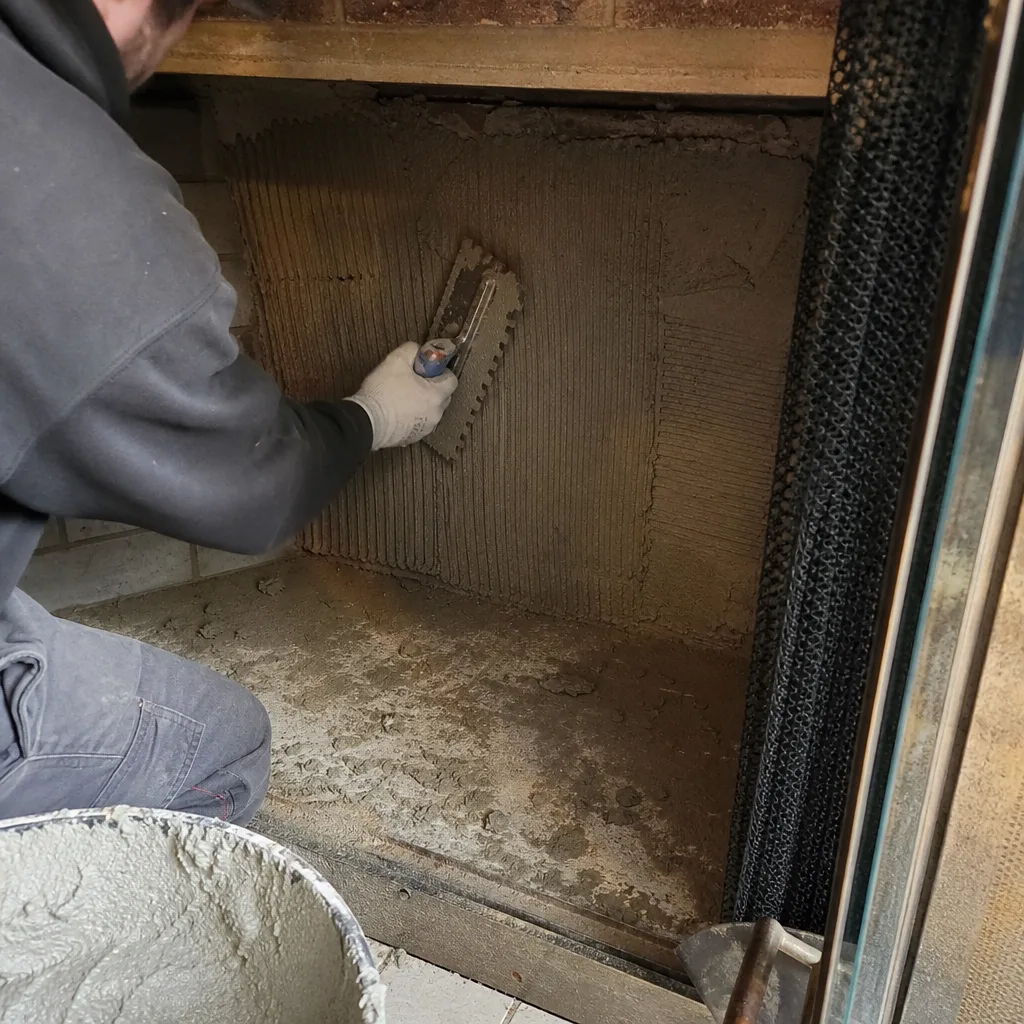 Tradesperson applying mortar with a notched trowel inside a fireplace